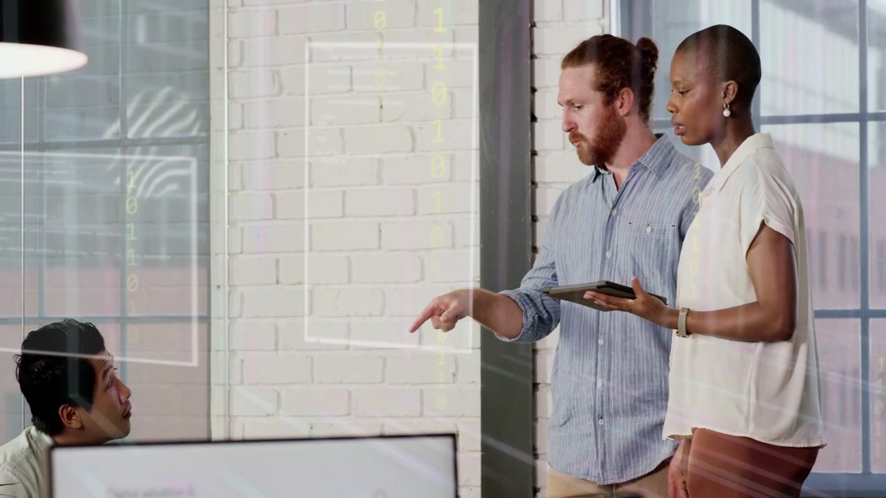 Standing woman showing tablet and bearded man reviewing data at desk with HUD overlay, planning