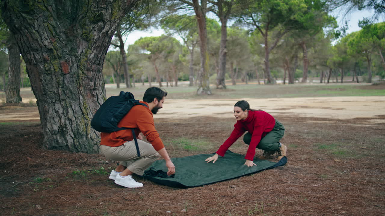 una pareja feliz extendiendo una manta en el bosque de hierba. una pareja preparando un lugar para picnic.