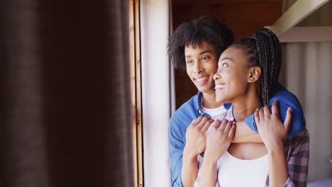 Feliz-Pareja-Afroamericana-Mirando-Por-La-Ventana-Y-Abrazándose-En-Una-Cabaña-De-Madera,-Cámara-Lenta