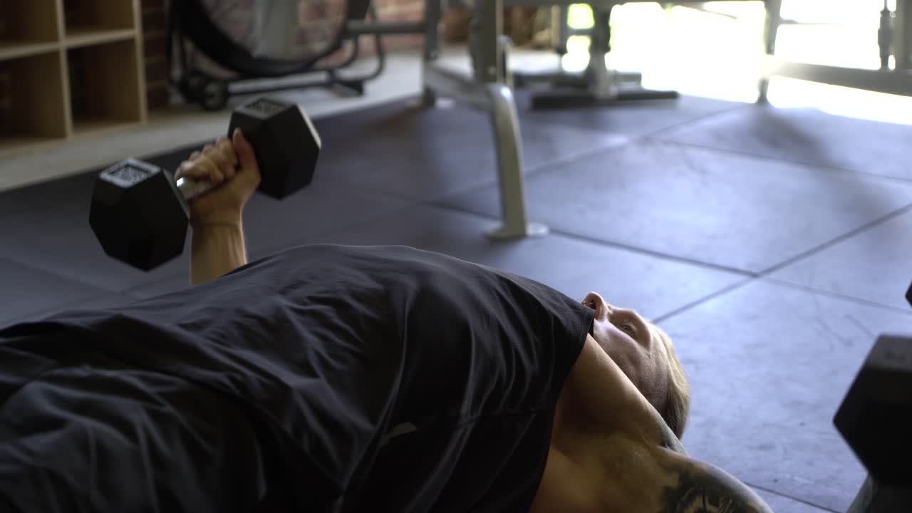 hombre tatuado en el gimnasio en casa cerrar declive moscas en el pecho con mancuernas