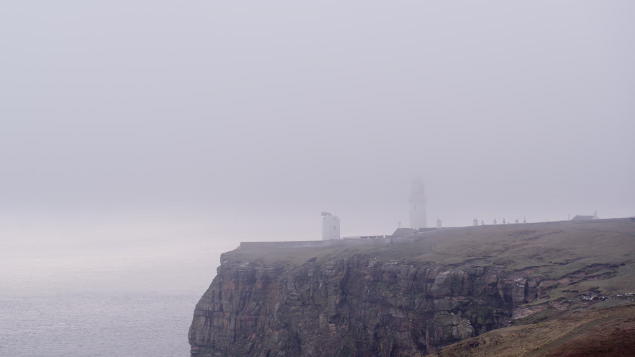 disparo aéreo de un faro cubierto de niebla en la parte superior de un acantilado en una mañana brumosa