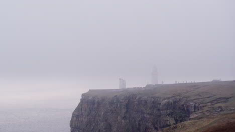 disparo aéreo de un faro cubierto de niebla en la parte superior de un acantilado en una mañana brumosa