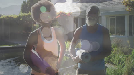 animation of light spots over african american couple holding yoga mats, slow motion