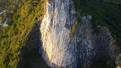 4k-Top-down-Aerial-pan-around-carved-Buddha-Image-made-from-Gold-on-a-cliff-at-Khao-Chee-Chan,-Pattaya,-Thailand