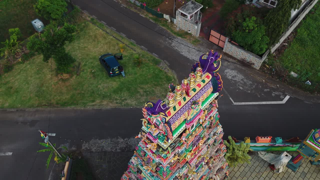 Aerial top of Tamil temple complex surrounded by trees showing colorful roof patterns and towers, orbit