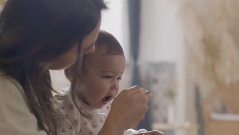 Happy-Beautiful-Woman-Sitting-At-Kitchen-Table-And-Feeding-Her-Baby-Daughter-With-Apple-Puree