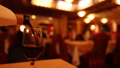 Hand pours red wine into glass on table in warmly lit, upscale restaurant interior