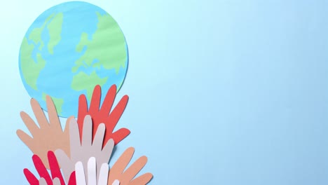 Close-up-of-hands-together-with-globe-made-of-colourful-paper-on-blue-background-with-copy-space