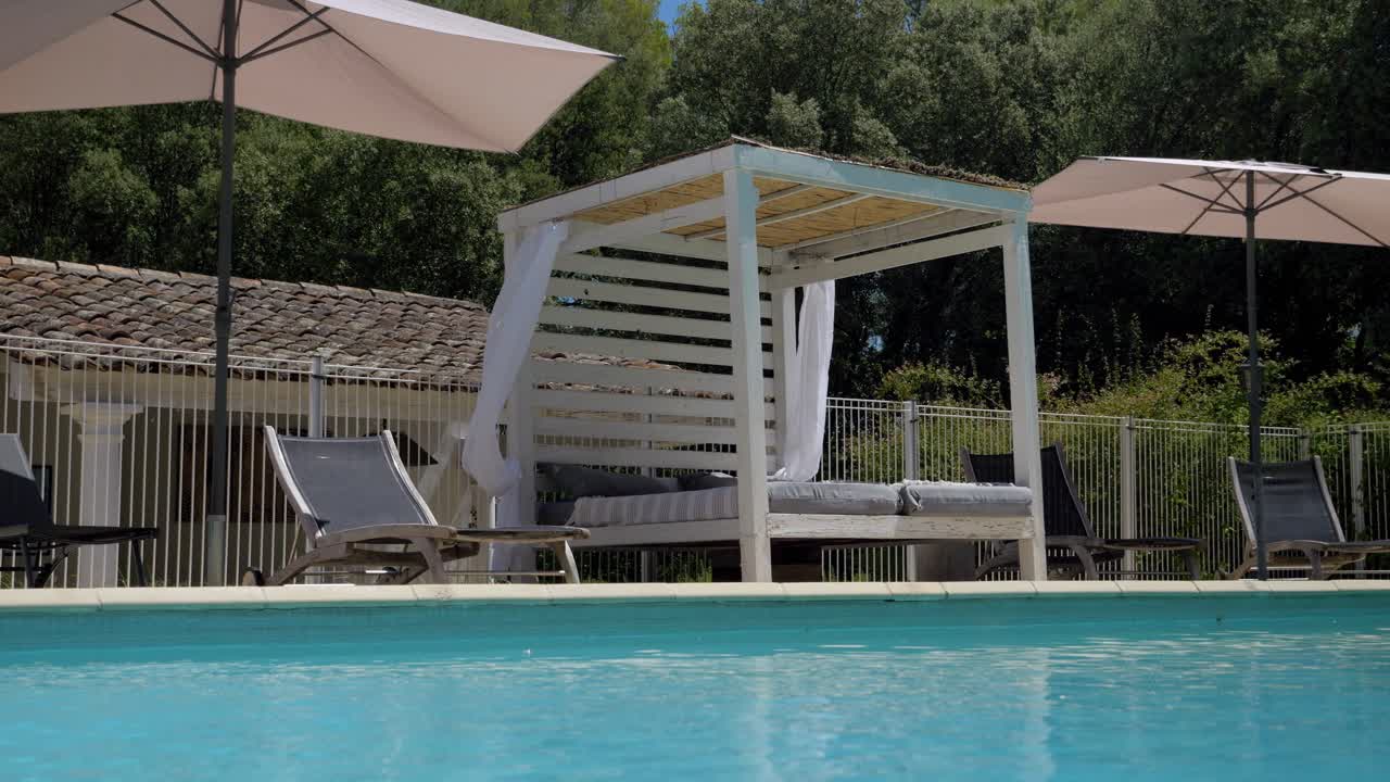 Langsomt oversigtsskud af en solseng med svævende gardiner ved siden af en privat pool