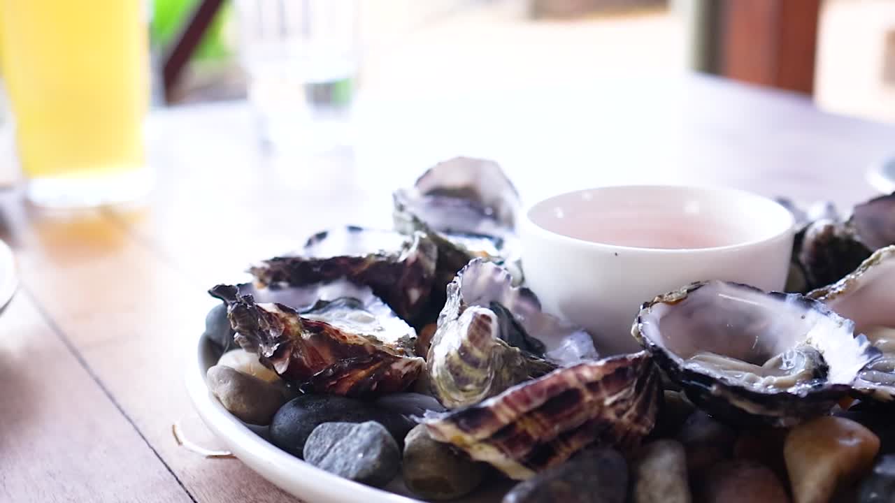 A person's hand reaches for a fresh oyster from a platter on a wooden table