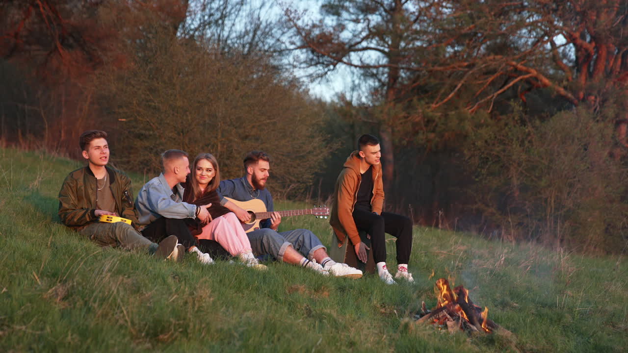 Friends playing guitar near a campfire