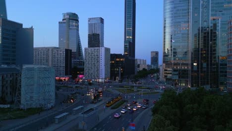 Vista-Aérea-Del-Centro-De-La-Ciudad-De-Varsovia-Durante-La-Hora-Azul,-Dando-Vueltas-Alrededor-De-Rondo-Onz-Con-Modernos-Edificios-De-Oficinas-Y-Reflejos-Impresionantes