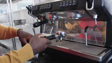 midsection of african american male baker making coffee in bakery, slow motion