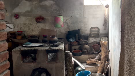 inside rural rustic old kitchen in countryside region, cement traditional wood coal fire stove cooktop, dishes pans pots and pottery scattered around, interior antique and poverty, dolly view