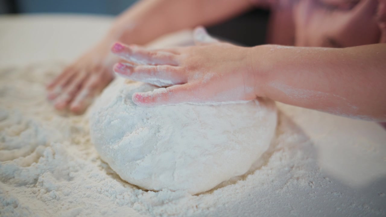 Close-up of hands kneading dough in flour. Flour dusts fingers and surface. Hands work steadily, focused on shaping dough. Ideal for cooking, baking, or culinary projects