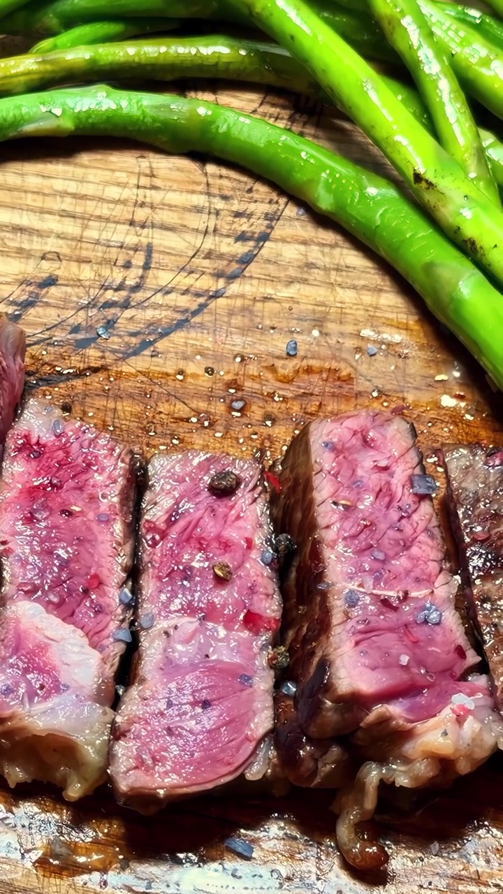 Handheld vertical close-up of juicy sliced medium-rare steak with green asparagus on a wooden board, perfect for rustic culinary and gourmet food marketing