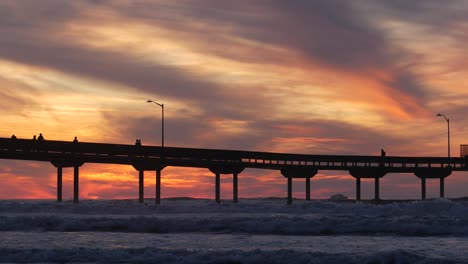 surfers surfing by pier. ocean water waves, people and sky at sunset. california