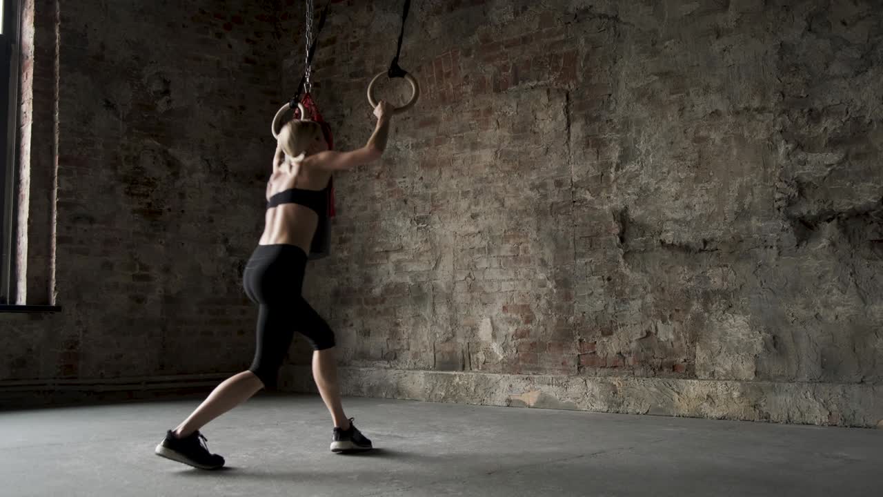 스포츠 링에서 플립을 하는 스포츠 소녀. 체조 링에서 스트레칭을 하는 젊은 건강한 여성. 체육관에서 링으로 운동하는 근육성 젊은 여성 운동선수. 체육 링에서 풀업을하는 젊은 건강한 여자