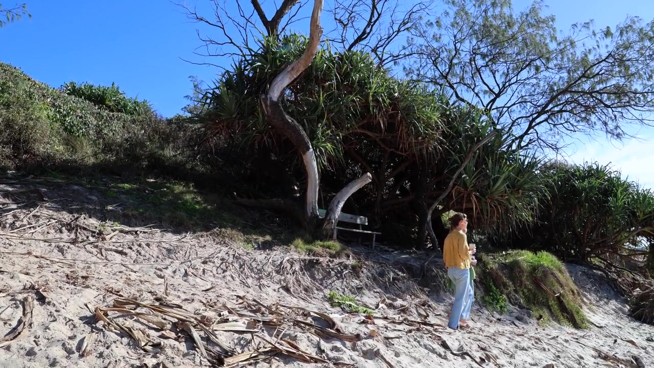 Dos mujeres jóvenes caminando descalzas por un sendero costero arenoso