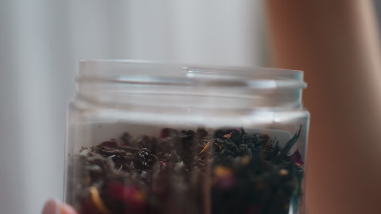 Caucasian Woman Picking Loose Tea Jar Fingertips Dip Into Glass Container Retrieving Dried Leaves, CloseUp Of Tactile Selection And Aroma Discovery, Relaxed Morning Tea Routine In Home Kitchen