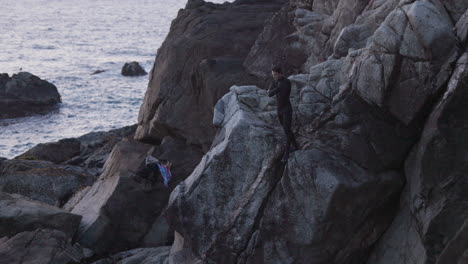 Adult-male-climbs-cliff-and-cliff-jumps-off-into-the-ocean-at-sunset