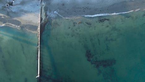 green blue ocean water waves crash peacefully on sandy shoreline by seawall