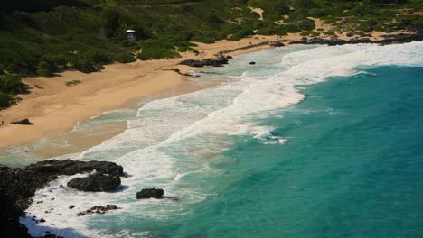 Grandes-Olas-Rodando-En-La-Costa-Este-De-Oahu-En-Verano-Con-Playa-De-Arena,-Roca-Volcánica-Negra-Y-Algunos-Turistas