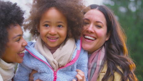 Portrait-Of-Family-With-Two-Mums-Outdoors-On-Walk-In-Autumn-Countryside-With-Daughter