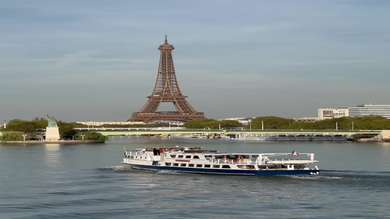 Vista ampia di una barca a vela lungo la Senna con la Torre Eiffel sullo sfondo sotto un cielo limpido. Tranquilla scena fluviale parigina che mette in risalto l'iconico monumento, il paesaggio urbano e la crociera turistica