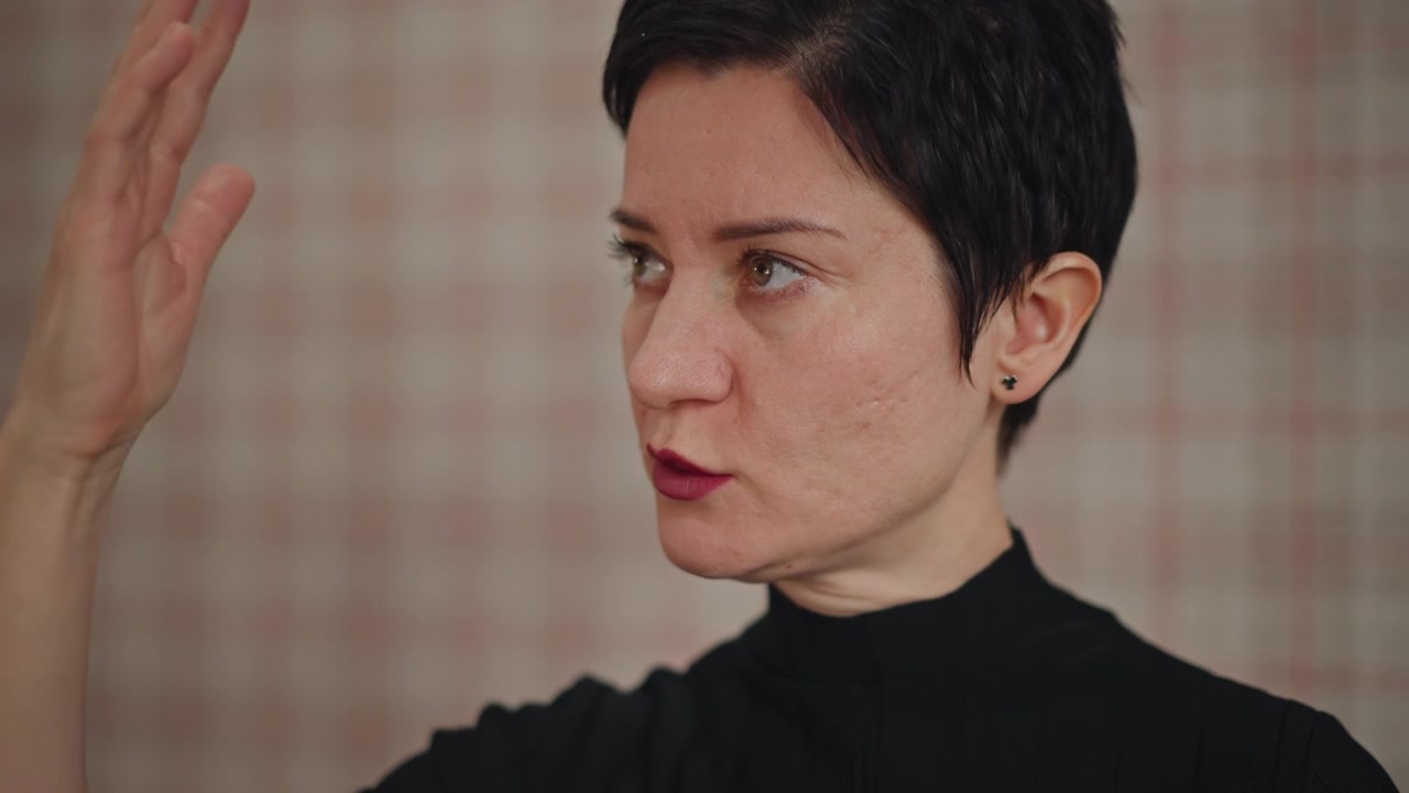 Ritratto ravvicinato di un'istruttrice di canto (vocal coach) concentrata, con capelli corti, su sfondo a quadri, che insegna tecnica di canto, gesti espressivi e dizione precisa, guidando fuori campo.