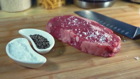 rib eye steak being seasoned on a chopping board