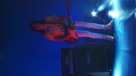 vertical video cheerful man jumping dancing and playing guitar in colored neon light smoke and spotlights in the studio on a changing background