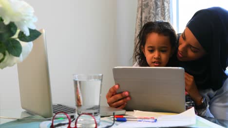 madre joven usando una tableta digital con su hija en la mesa 4k