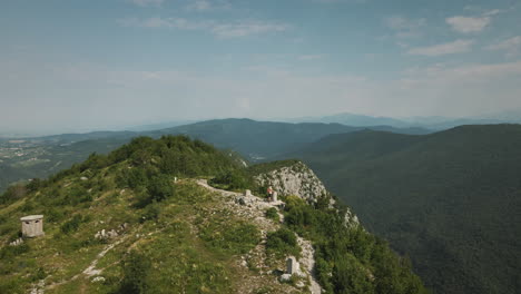 drone shot of the top of mountain sabotin where a hiker with an orange backpack stoped by a concrete monument