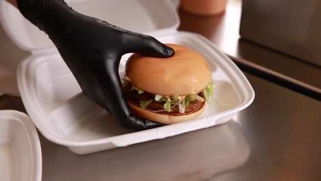 hand in black glove holding a burger in styrofoam box