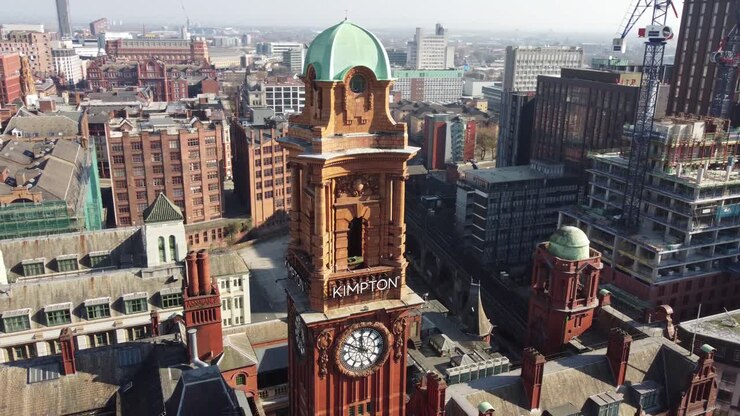 Aerial drone flight around the clock tower of the Refuge Building on Oxford Road in Manchester City Centre showing a view of the surrounding rooftops and new building being constructed
