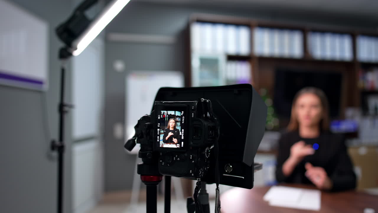Long-haired Caucasian female shooting video actively articulating and gesturing. Modern educational blogging. Blurred backdrop.