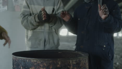 people warming hands around a barrel fire in an urban setting