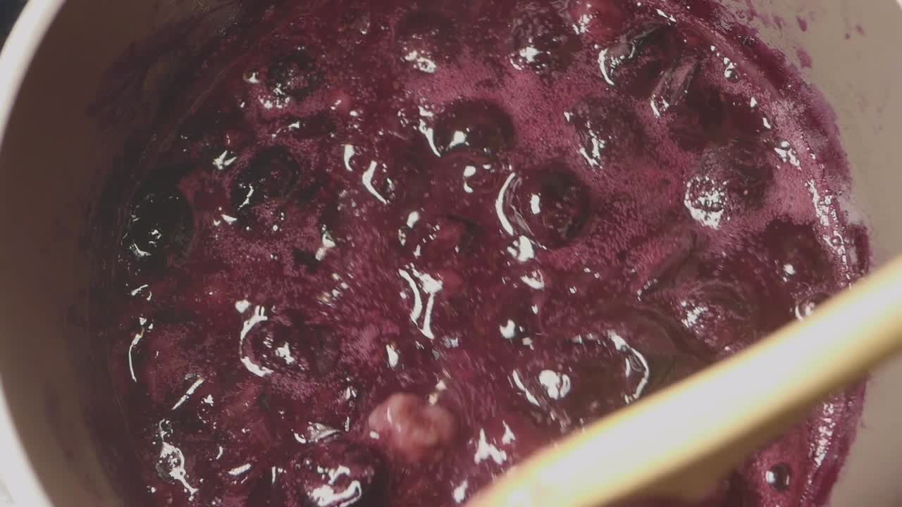 Stirring Boiling Berry Jam in a Pot with a Wooden Spoon