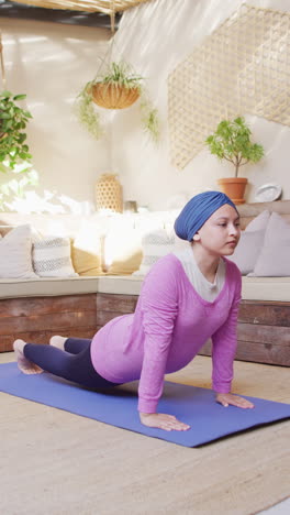 video of tranquil biracial woman in hijab stretching in yoga pose at home