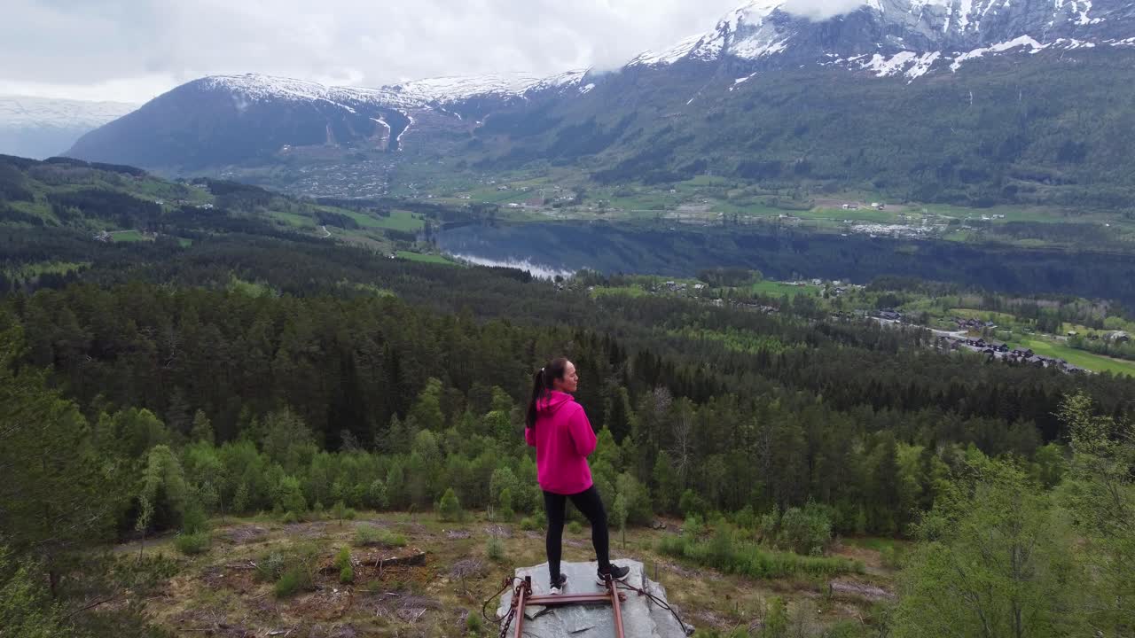 Woman standing on abandoned railway mining track viewpoint and looking towards lake Lonavatnet in Voss Norway - Forward moving aerial from Nordheim slate mine in Voss