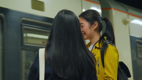 두 명의 젊은 여성 친구들이 지하철 역 플랫폼에서 기차를 기다리고 있습니다.