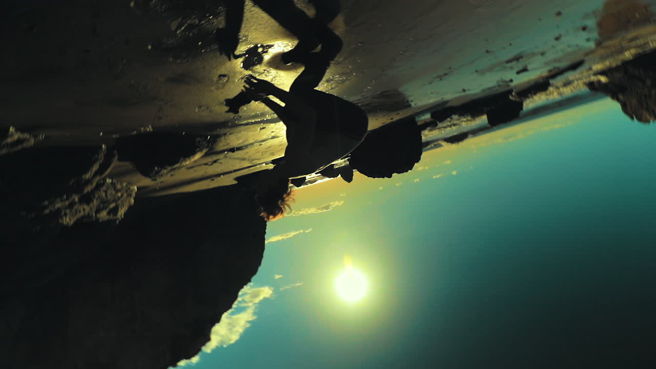 мужчина-спортсмен делает сальто назад на берегу пляжа в силуэте на фоне яркого солнечного света