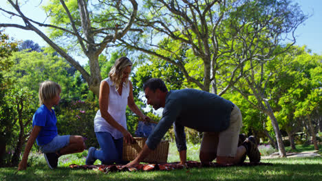 padre e hijo extendiendo la manta de picnic mientras la madre lleva la cesta 4k