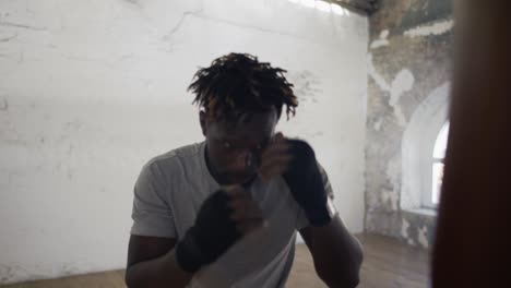 Confident-boxer-punching-the-heavy-bag-in-the-gym-actively,-close-up