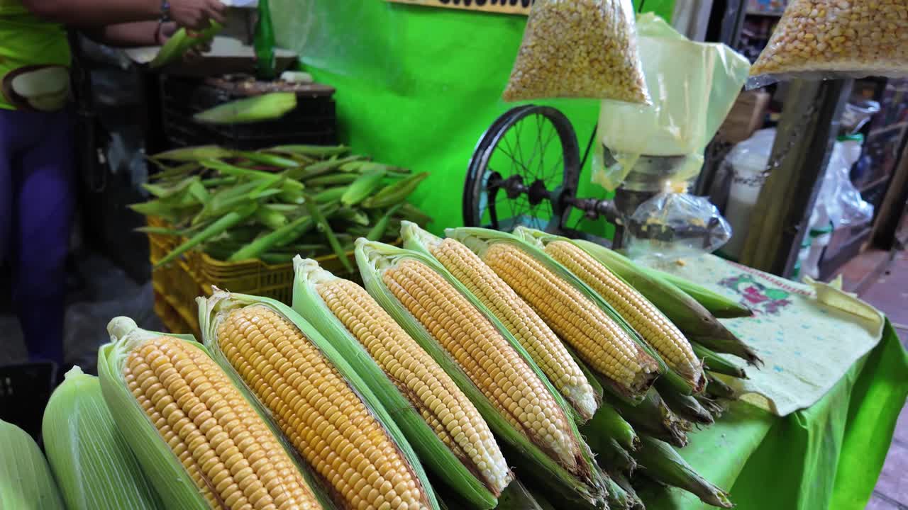 Fresh corn foreground, man peeling corn for cachapa in market backdrop