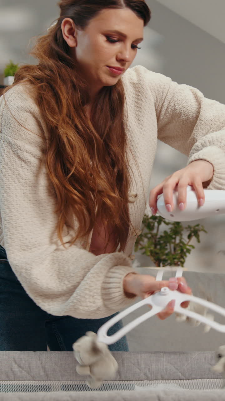 Pregnant woman carefully attaches stuffed animal mobile to crib preparing nursery for babys arrival