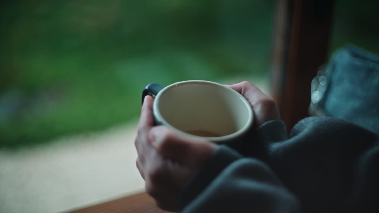 Person holding a cup of tea by the window
