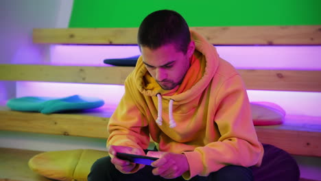 joven jugando a un juego móvil en una habitación colorida