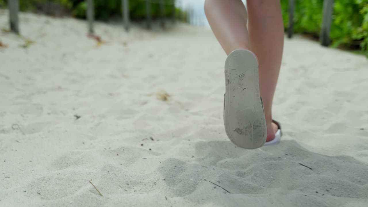 Kvindefødder med sandaler, der går i blødt sand i slowmotion